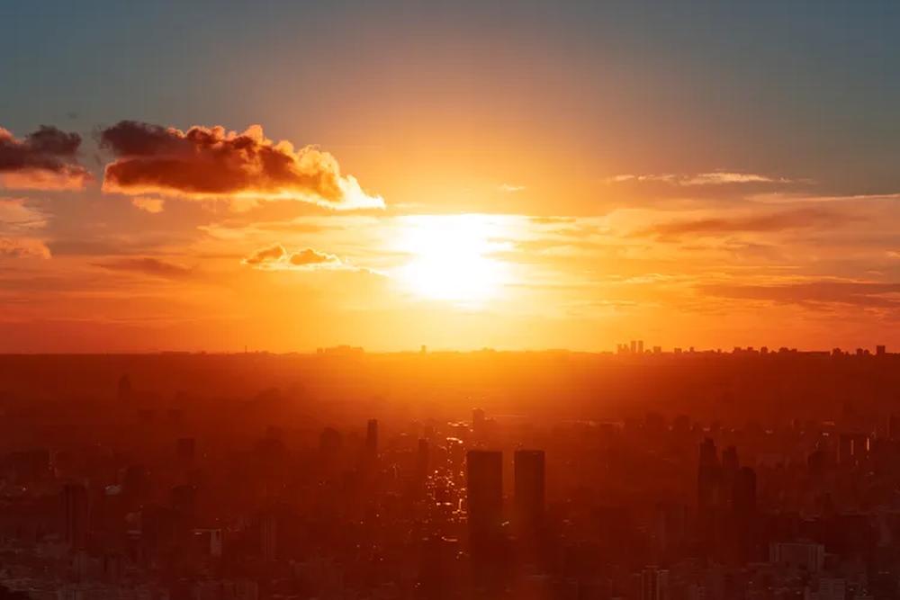 Image d’un coucher de soleil urbain vibrant avec un ciel orange et des gratte‑ciel en silhouette.