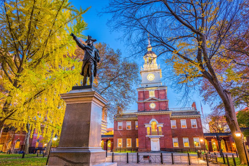 Image of Independence Hall in Philadelphia at twilight with the George Washington statue and autumn foliage in the foreground.