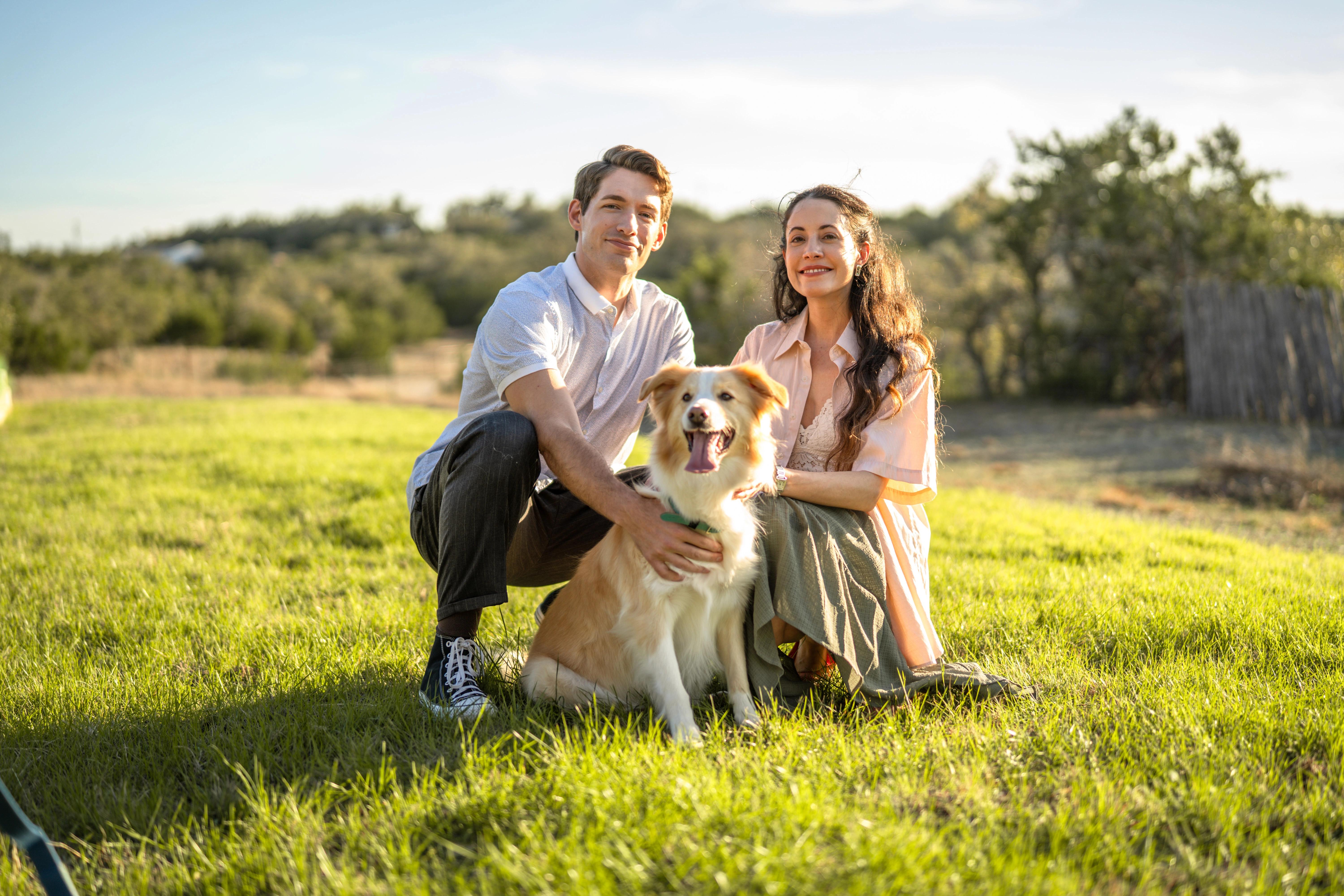 A couple playing outside on a sunny day with their golden dog tugging on a toy in a grassy yard.