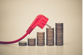 Red electrical plug leaning against stacks of coins symbolizing rising energy costs