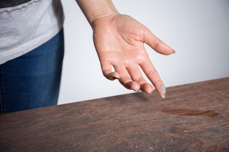 Image of a hand collecting dust on a wooden surface.