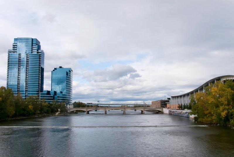 Cities Where Remote Workers Log the Most Hours - Images of the Grand Rapids, Michigan skyline with modern glass buildings and the Grand River bridge, featuring a calm and scenic waterfront.