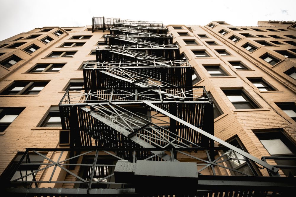 Upward view of a black metal fire escape on a tan brick apartment building.