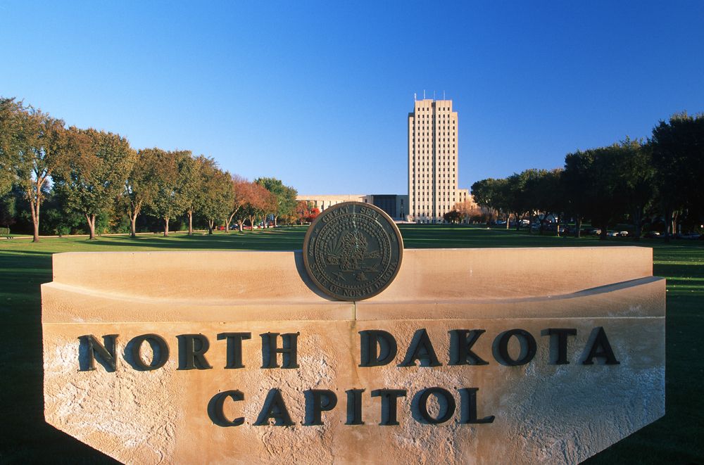 Tall government building in the distance behind a stone monument in a landscaped park.