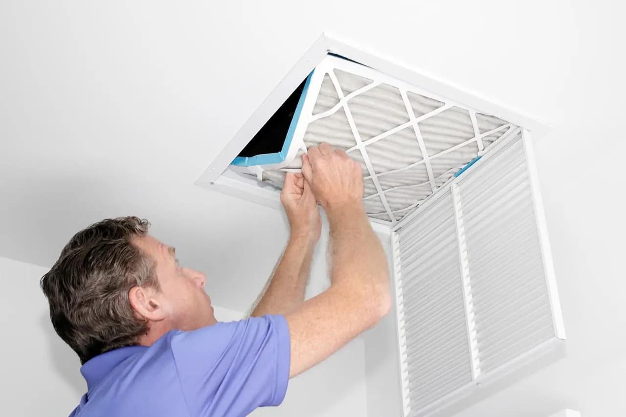 Man replacing a ceiling return air filter in a residential HVAC system.