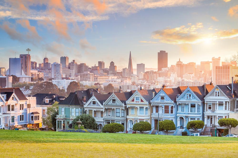 Iconic Painted Ladies Victorian homes with San Francisco skyline and Transamerica Pyramid at sunset.