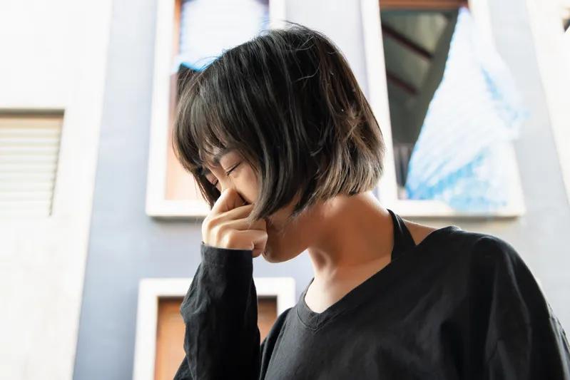 Vue d’une femme se bouchant le nez à l’extérieur, réagissant à une forte odeur ou à des COV en suspension dans l’air.