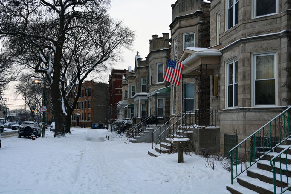 Snow-covered residential neighborhood with American flag and brownstone homes in Chicago during winter