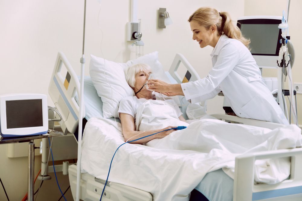 Nurse assisting an elderly female patient in a hospital bed by offering her an oxygen mask.