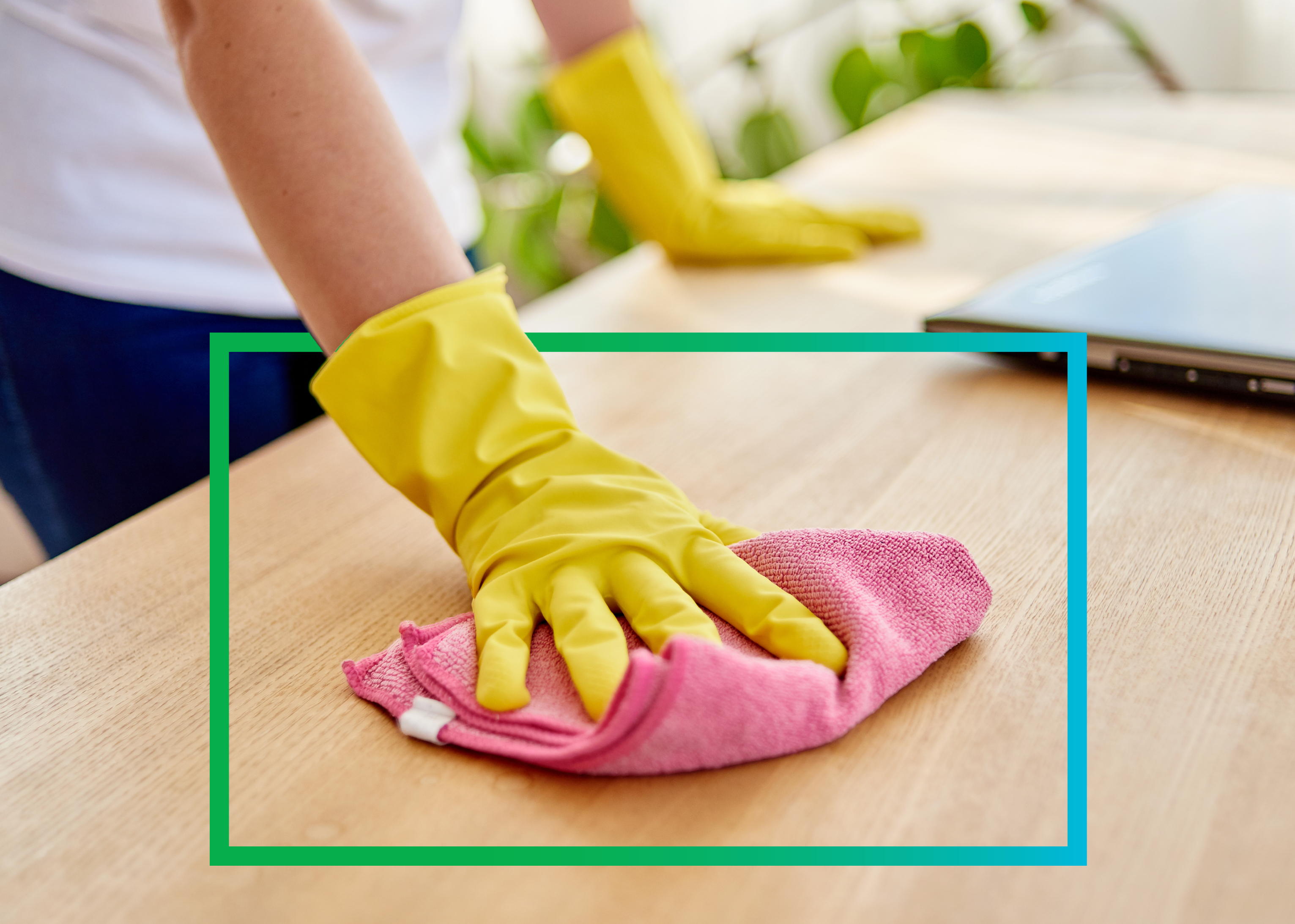 Person wearing yellow gloves wiping a wooden surface with a pink microfiber cloth.
