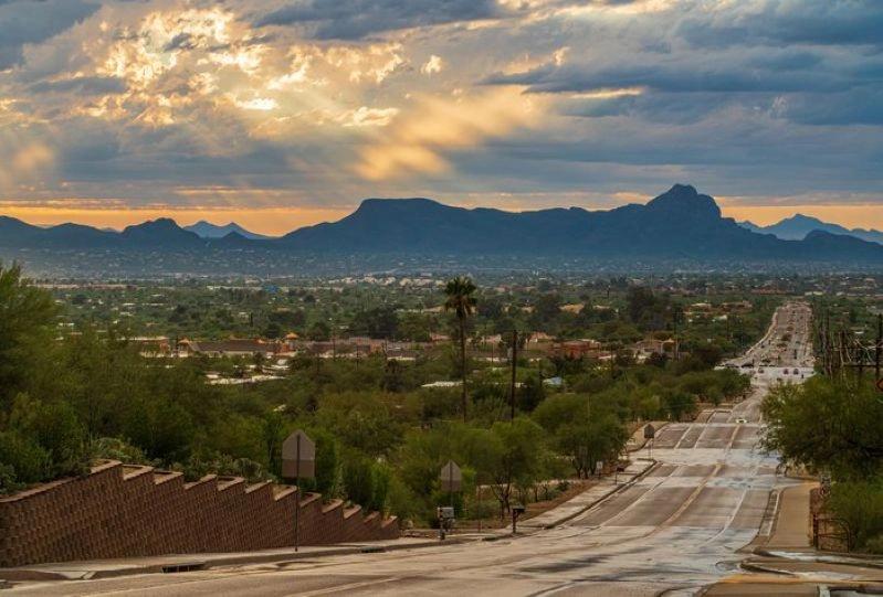 Cities Where Remote Workers Log the Most Hours - Images of the Tucson, Arizona landscape with a road leading towards the desert mountains, lit by rays of sunlight breaking through the clouds.