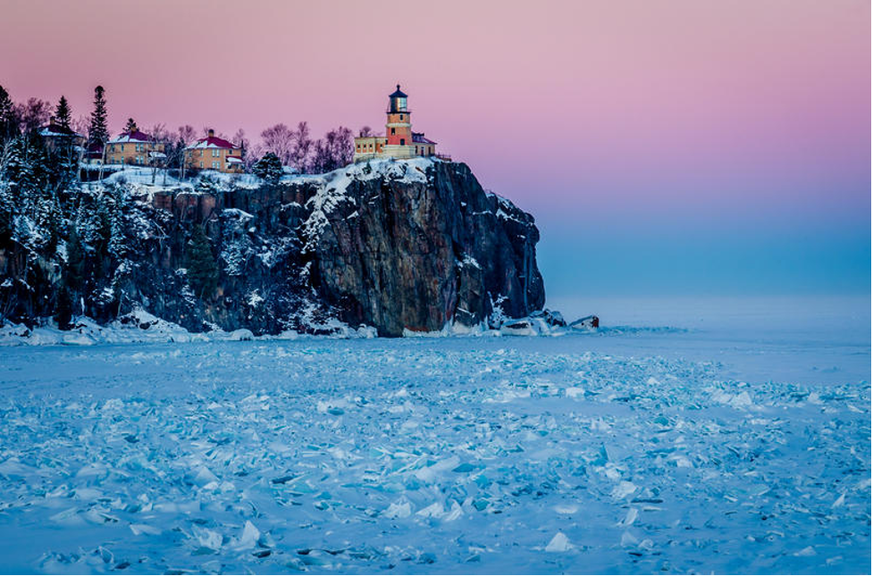 Split Rock Lighthouse perched on icy cliffs above a frozen Lake Superior during a colorful winter sunset in Minnesota