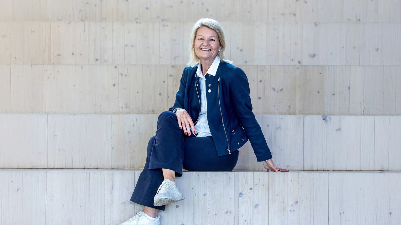 Rektor Anne Kristine Eggen Lervik fra Fagskolen Oslo sitter smilende på en tretrapp. Hun er kledd i en mørkeblå jakke og bukse, og hvite joggesko, mot en bakgrunn av lyse trepaneler.