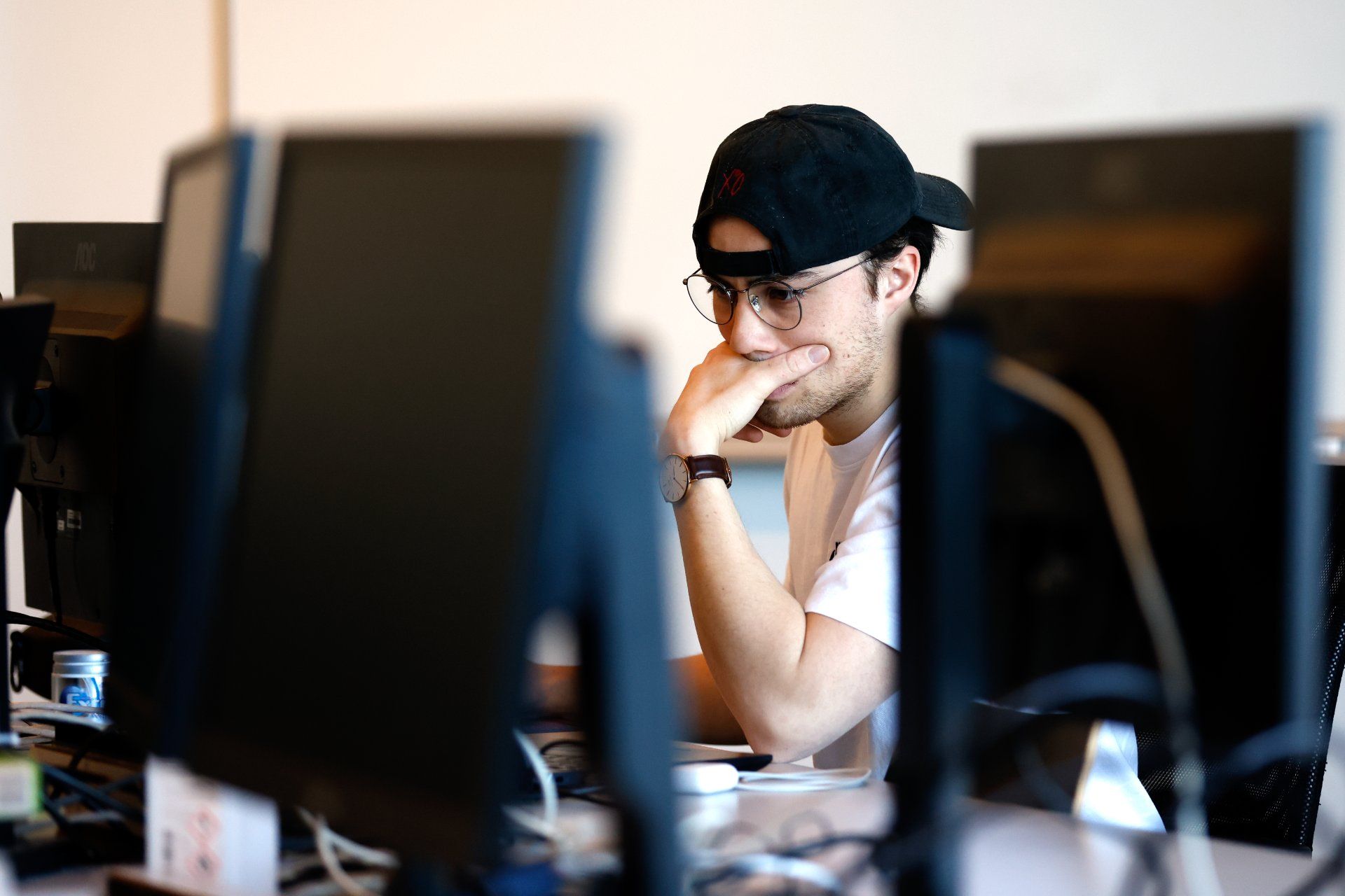 En konsentrert student sitter foran en dataskjerm i et klasserom, omringet av flere skjermer i et fokusert studiemiljø.