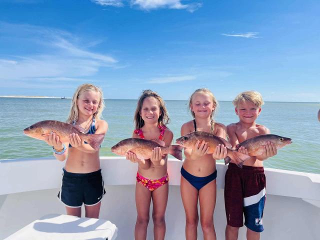 Four children holding snapper on a beach