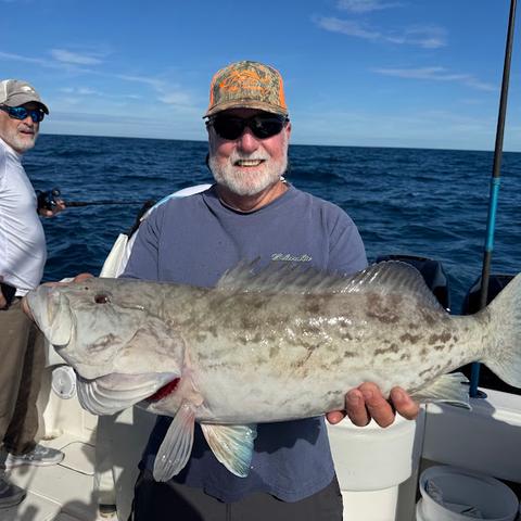 Angler in a camo cap holding a big gag grouper aboard Captain David White’s boat