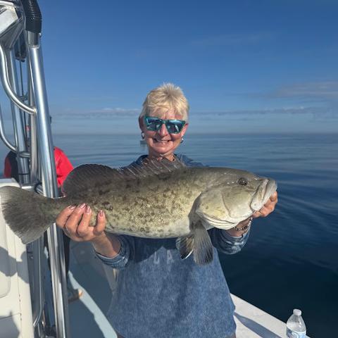 Smiling guest holding a gag grouper on a calm day aboard a Gulf fishing charter