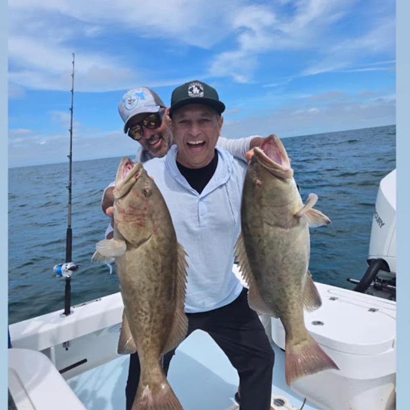 Grinning angler holding up two gag grouper, a full daily bag limit, on a Gulf fishing charter