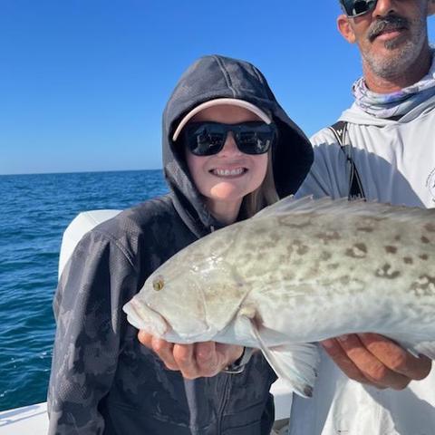 Charter guest in a hooded jacket holding a keeper gag grouper with Captain David White