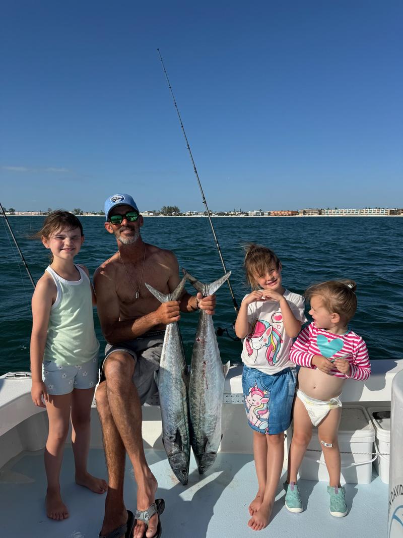 Four children and the captain with two king mackerel on a family fishing charter, Anna Maria Island shoreline behind
