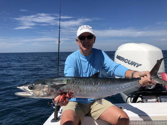 Angler in a white cap holding a king mackerel on a nearshore fishing charter off Anna Maria Island