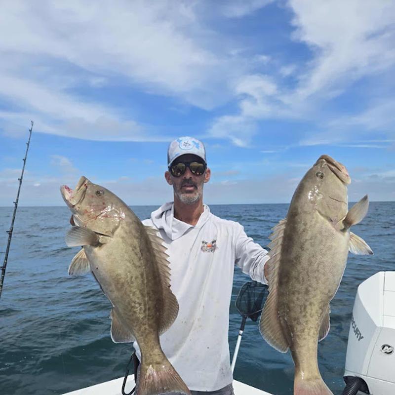 Captain David White holding a gag grouper in each hand after a nearshore trip in the Gulf of Mexico