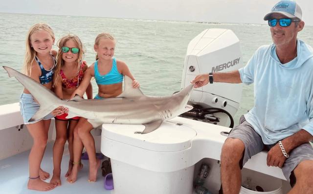Kids and Captain David holding a small shark on a boat