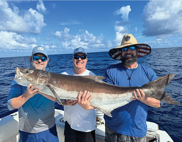 Three clients holding a large cobia
