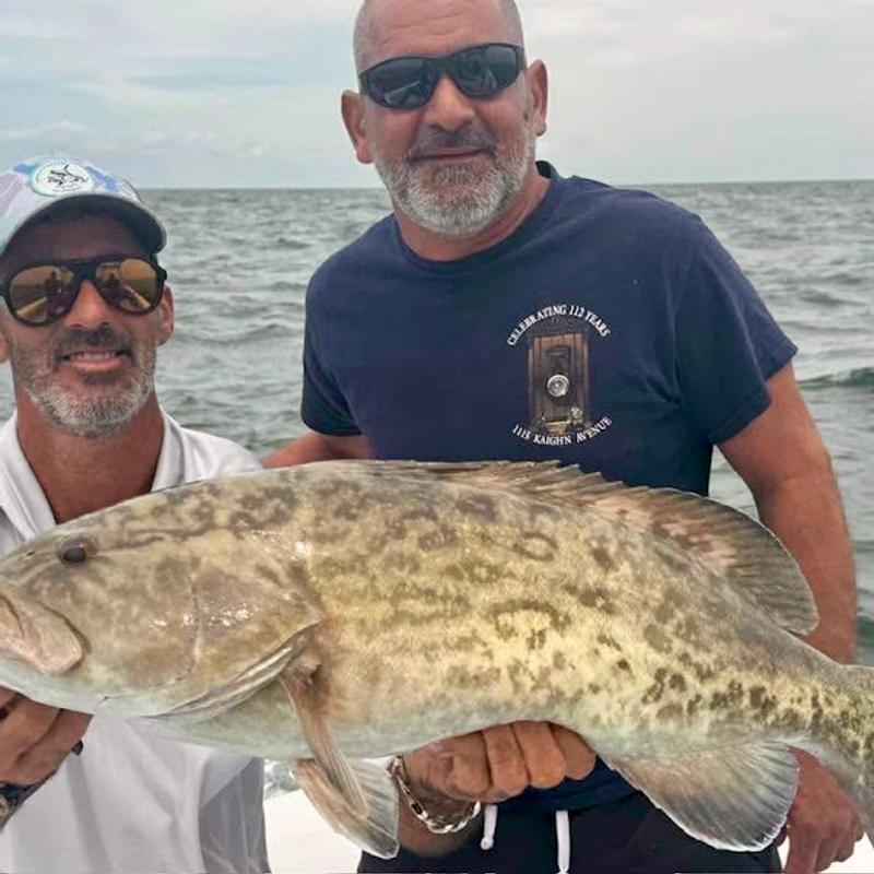 Charter guest and captain holding a large gag grouper across the deck of the boat