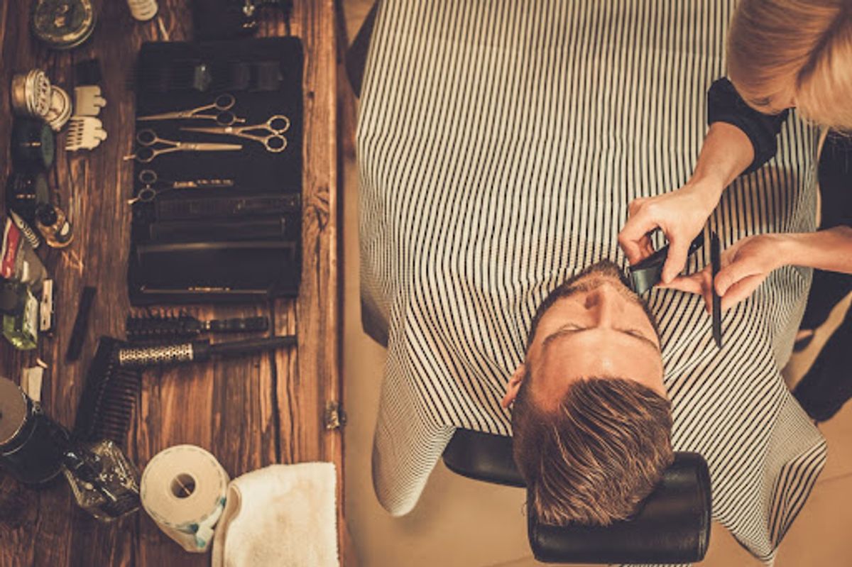 Barber trimming client's beard in shop.
