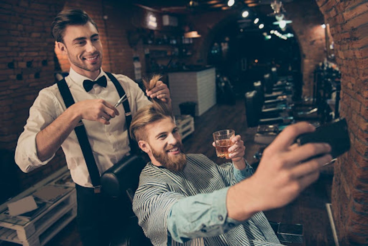Barber cutting client's hair, client taking a selfie.
