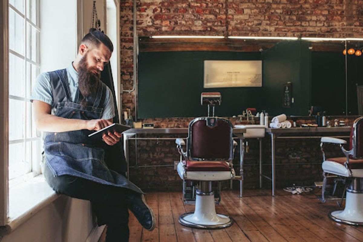Barber in apron using tablet in shop.