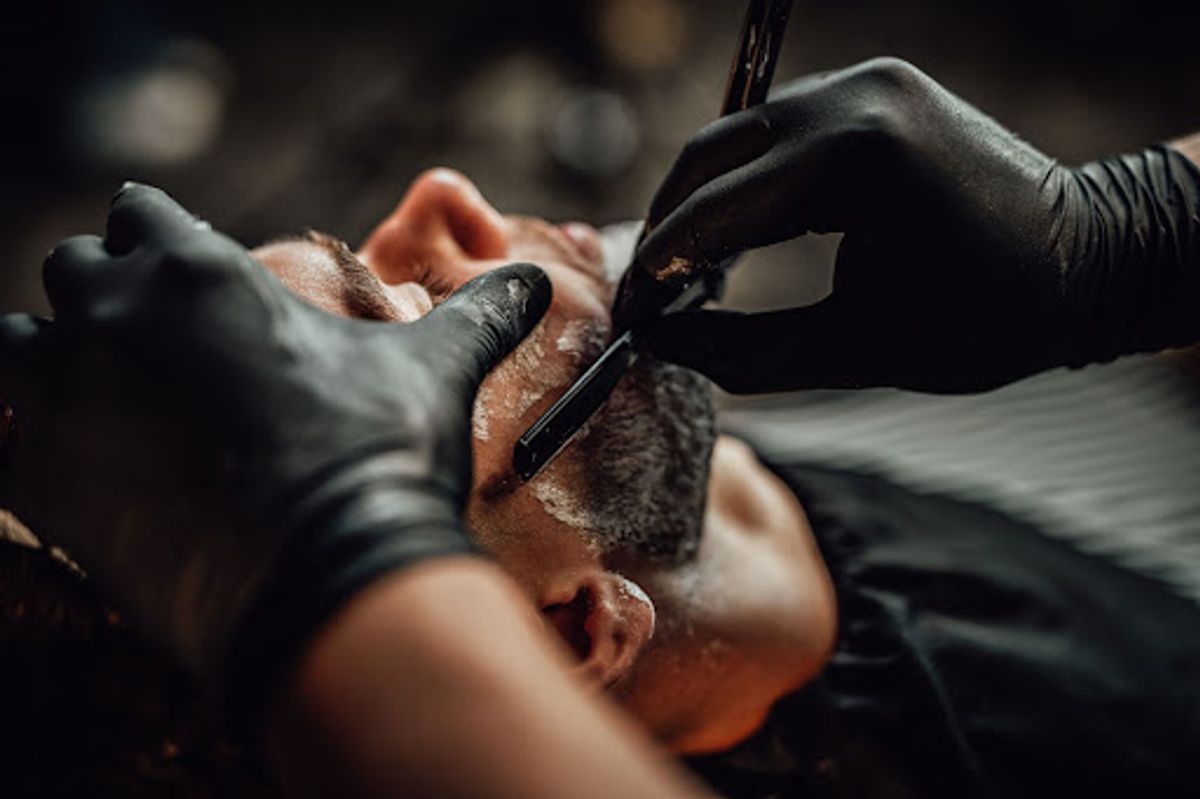 Barber shaping beard with a straight razor.