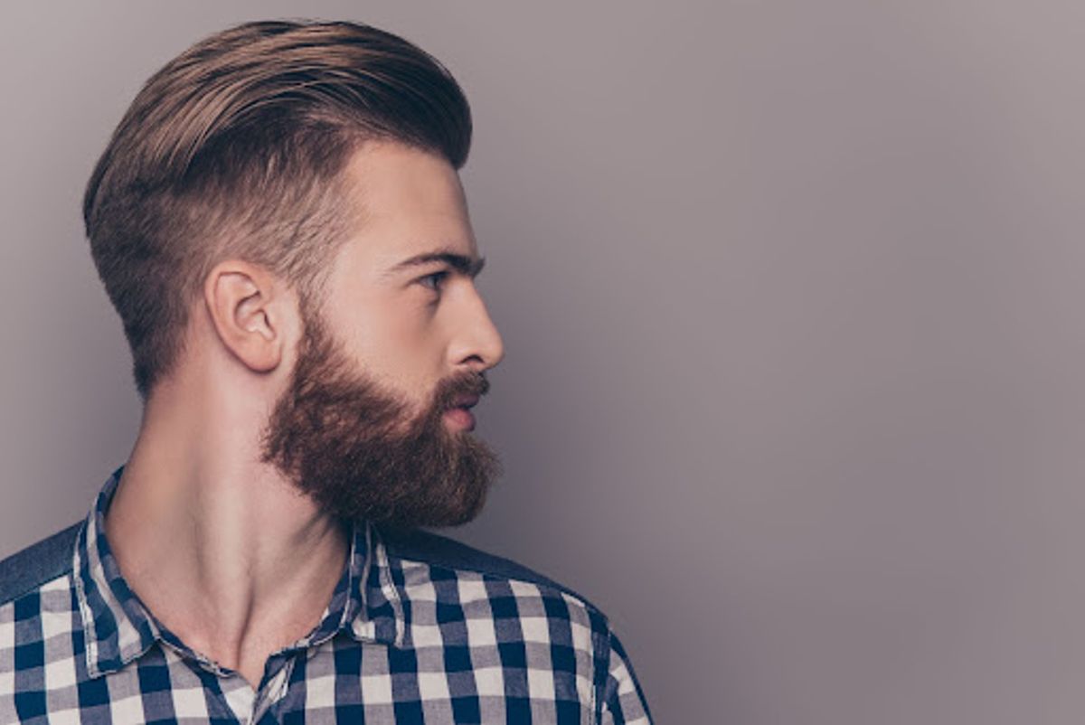 Hombre con peinado pompadour y barba mirando de lado.