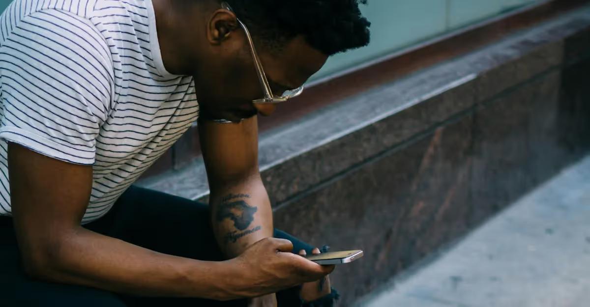 A person sitting on a bench looks down at a smartphone, appearing to book or check something.