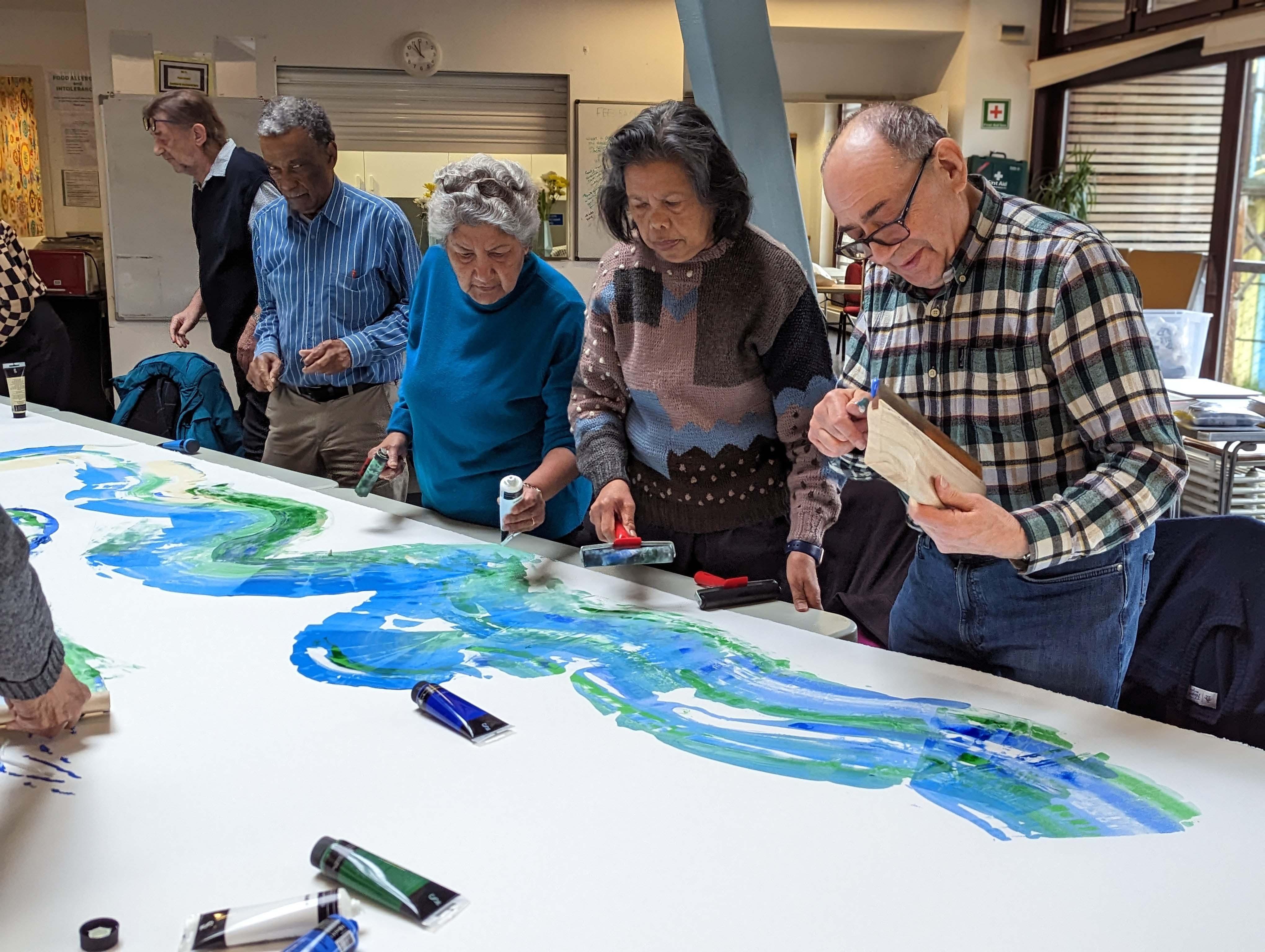 A group of four older people painting water on a single, large sheet of paper.