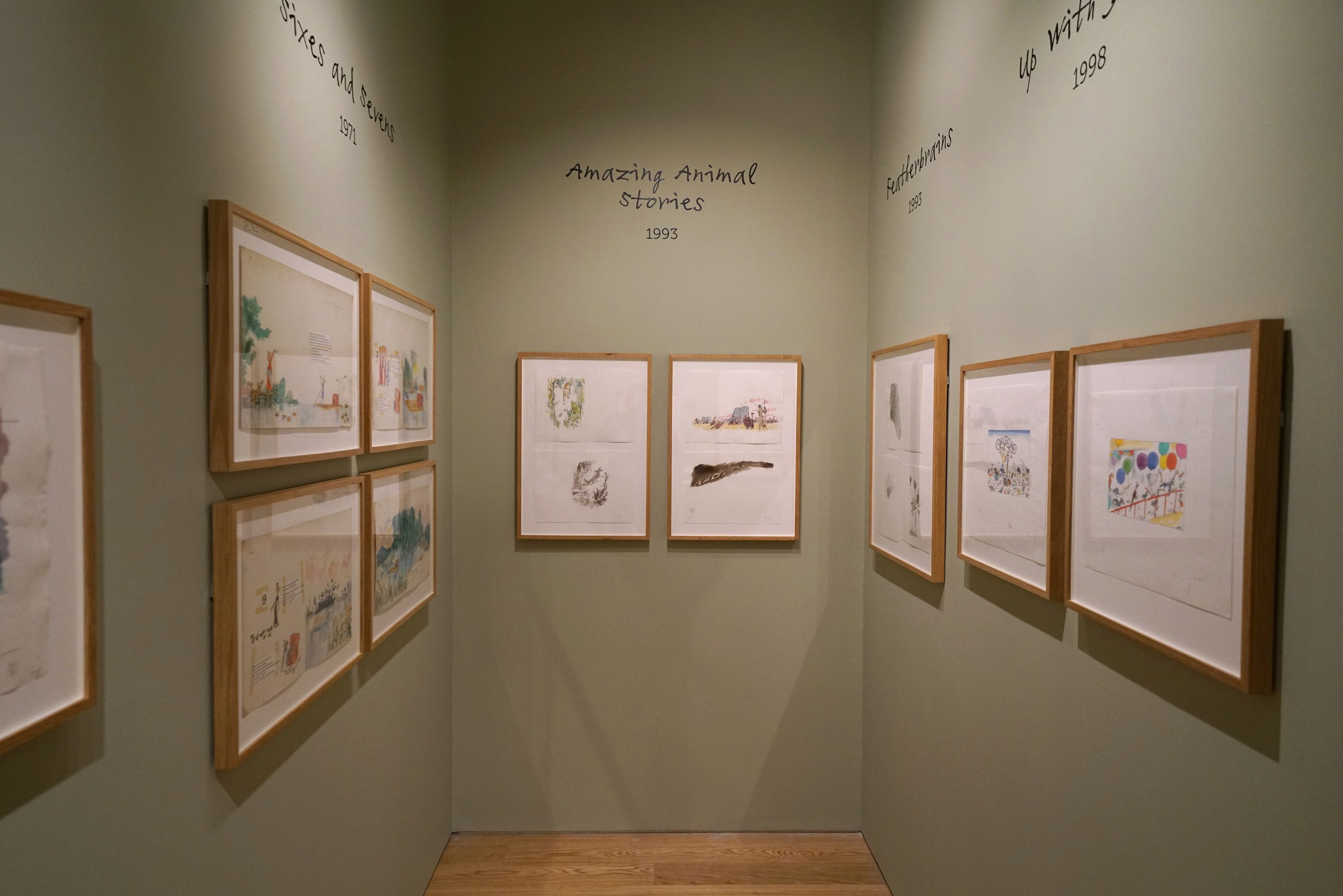 Framed illustrations displayed on a green wall in an exhibition space.