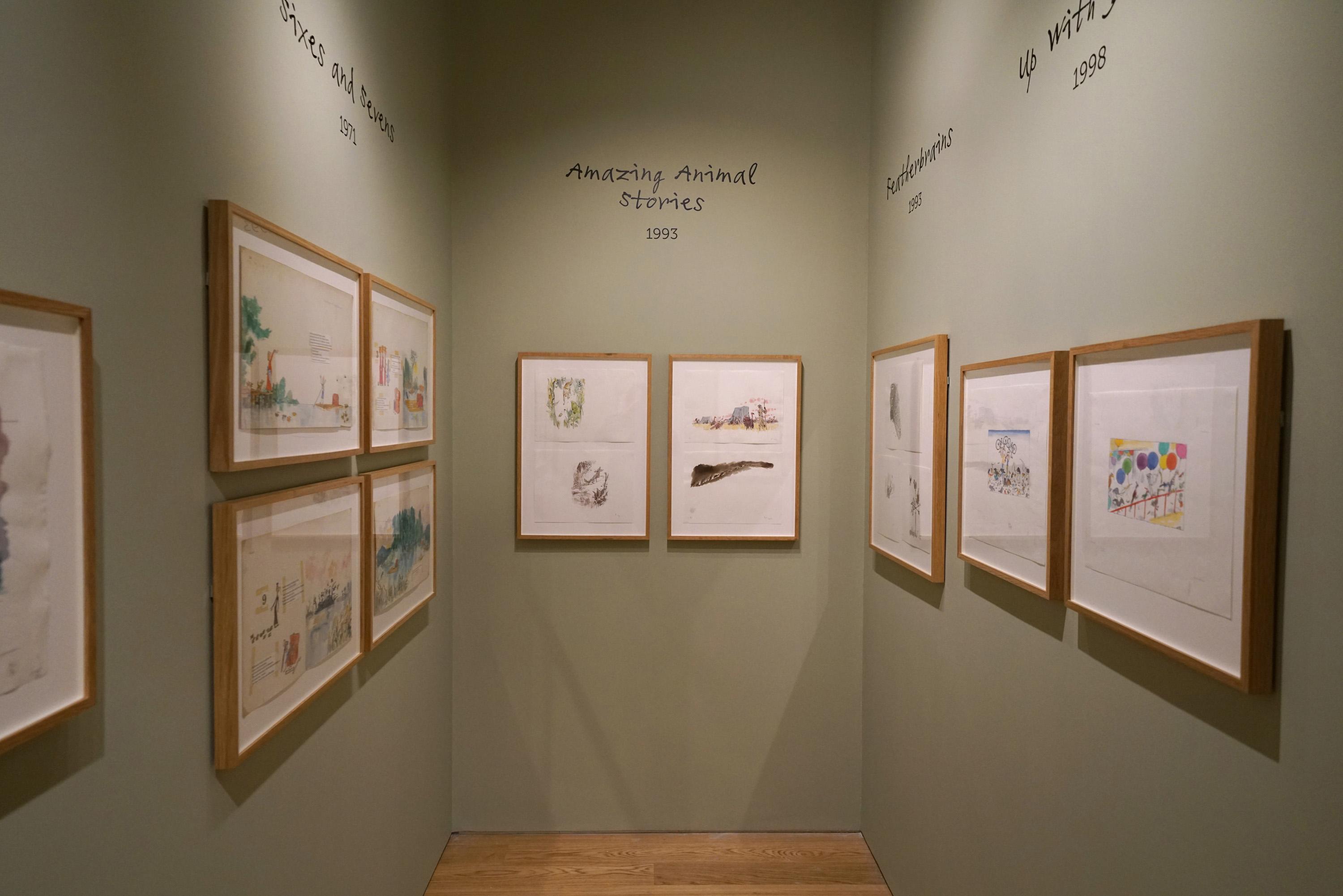 Framed illustrations displayed on a green wall in an exhibition space.