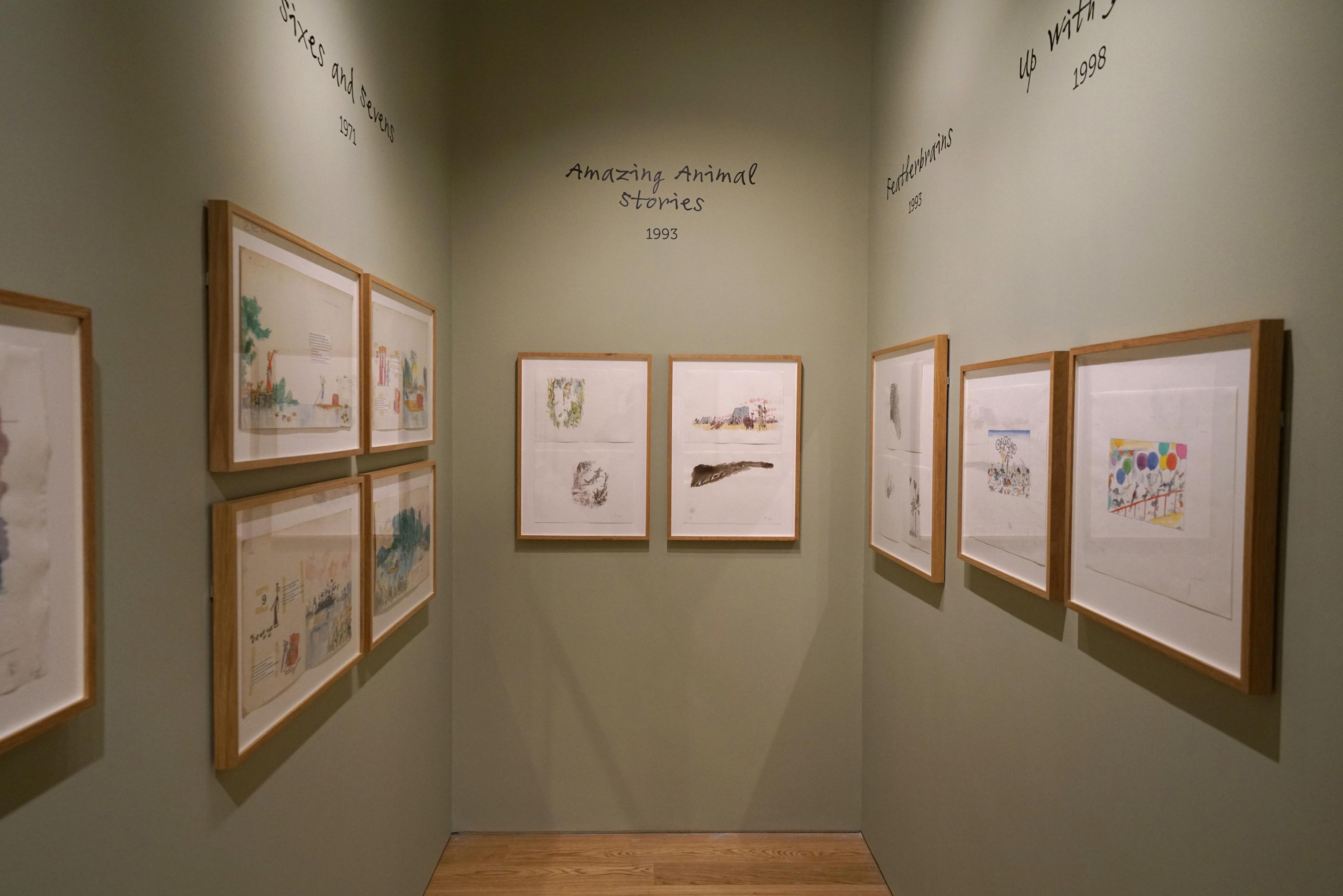 Framed illustrations displayed on a green wall in an exhibition space.