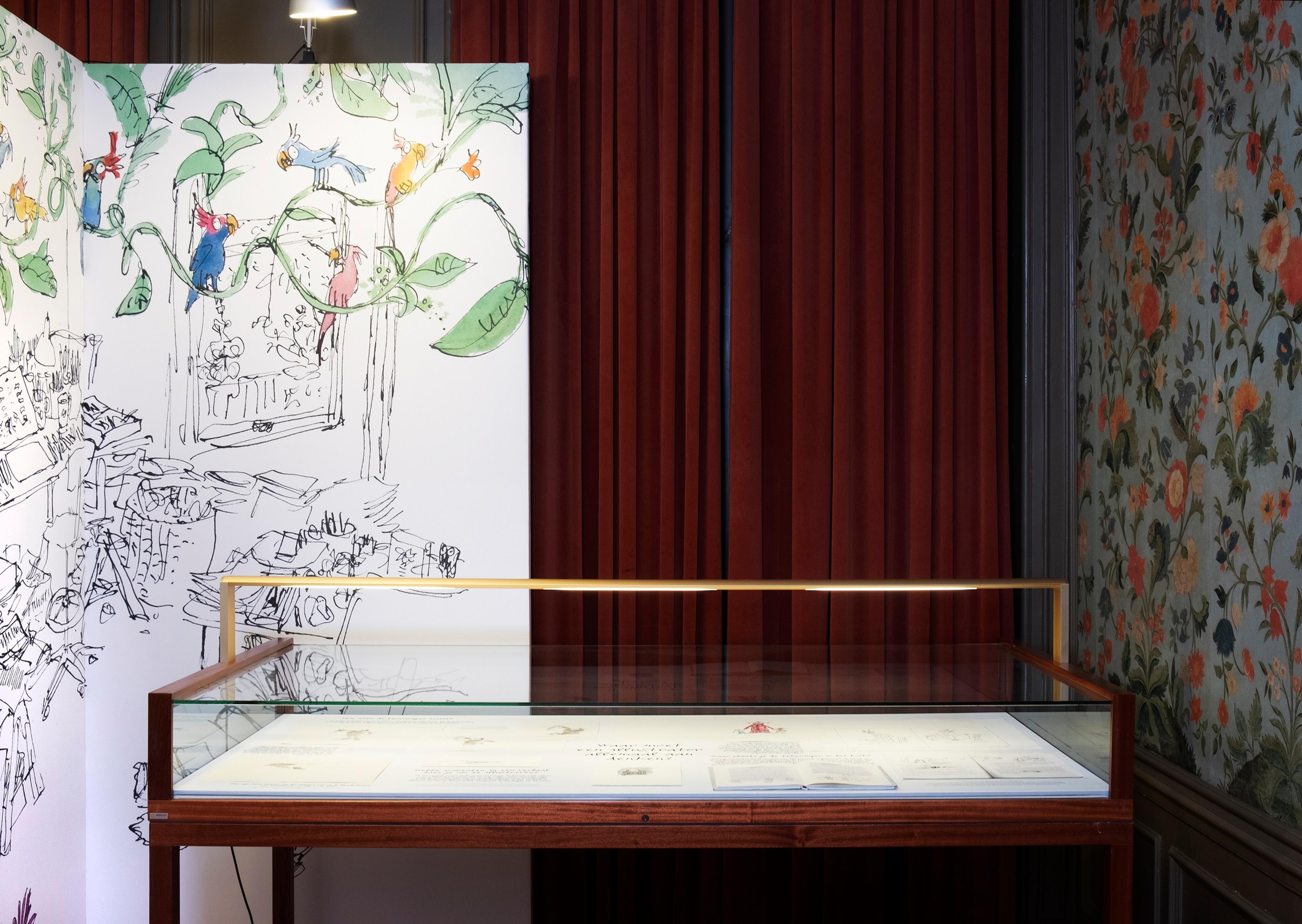 Exhibition photograph showing walls with decorative wallpaper, red velvet curtain and display case
