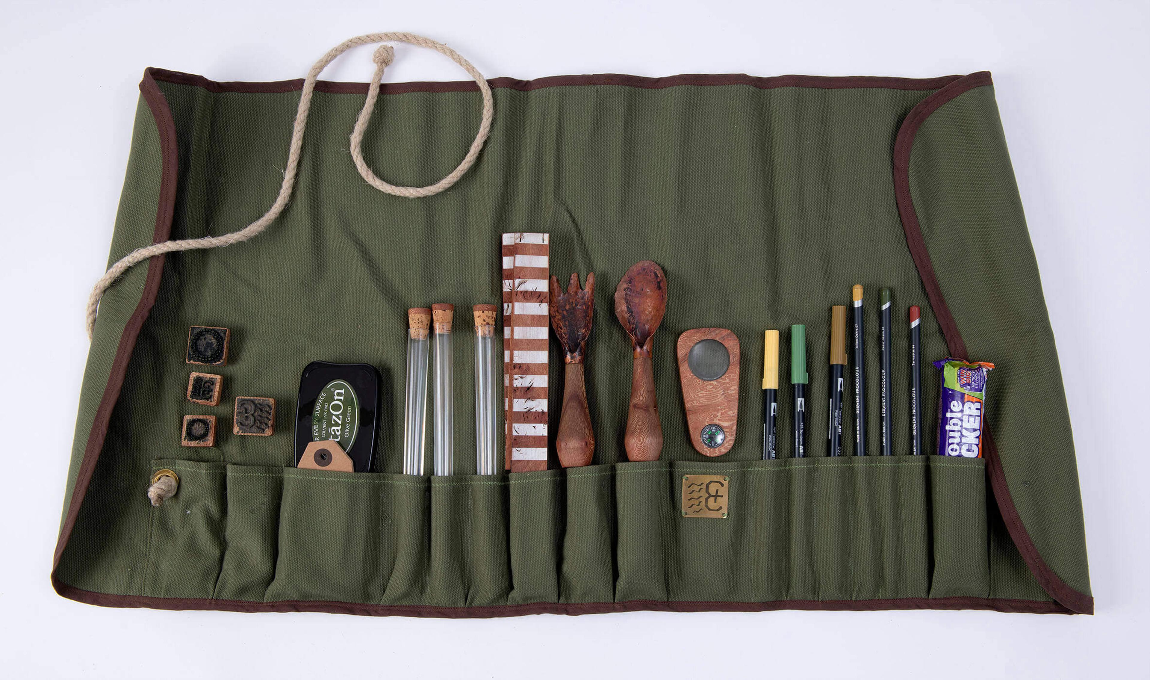 Photograph of green fabric tool roll with wooden stamps, test tubes, digging tools, a magnifying glass, a ruler, pens and a Double Decker chocolate bar