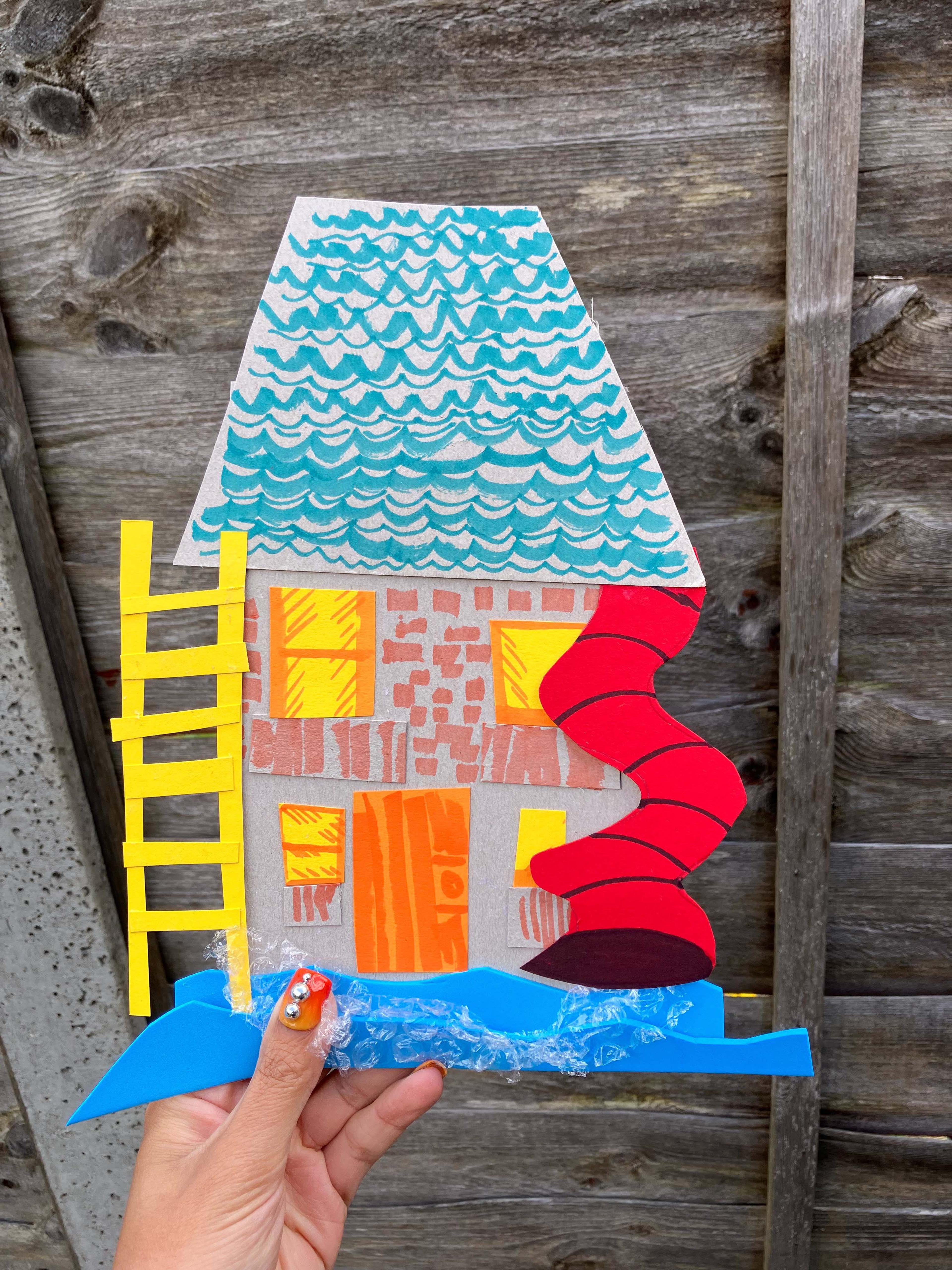 A hand holding up a collage of a house made from different recycled paper.