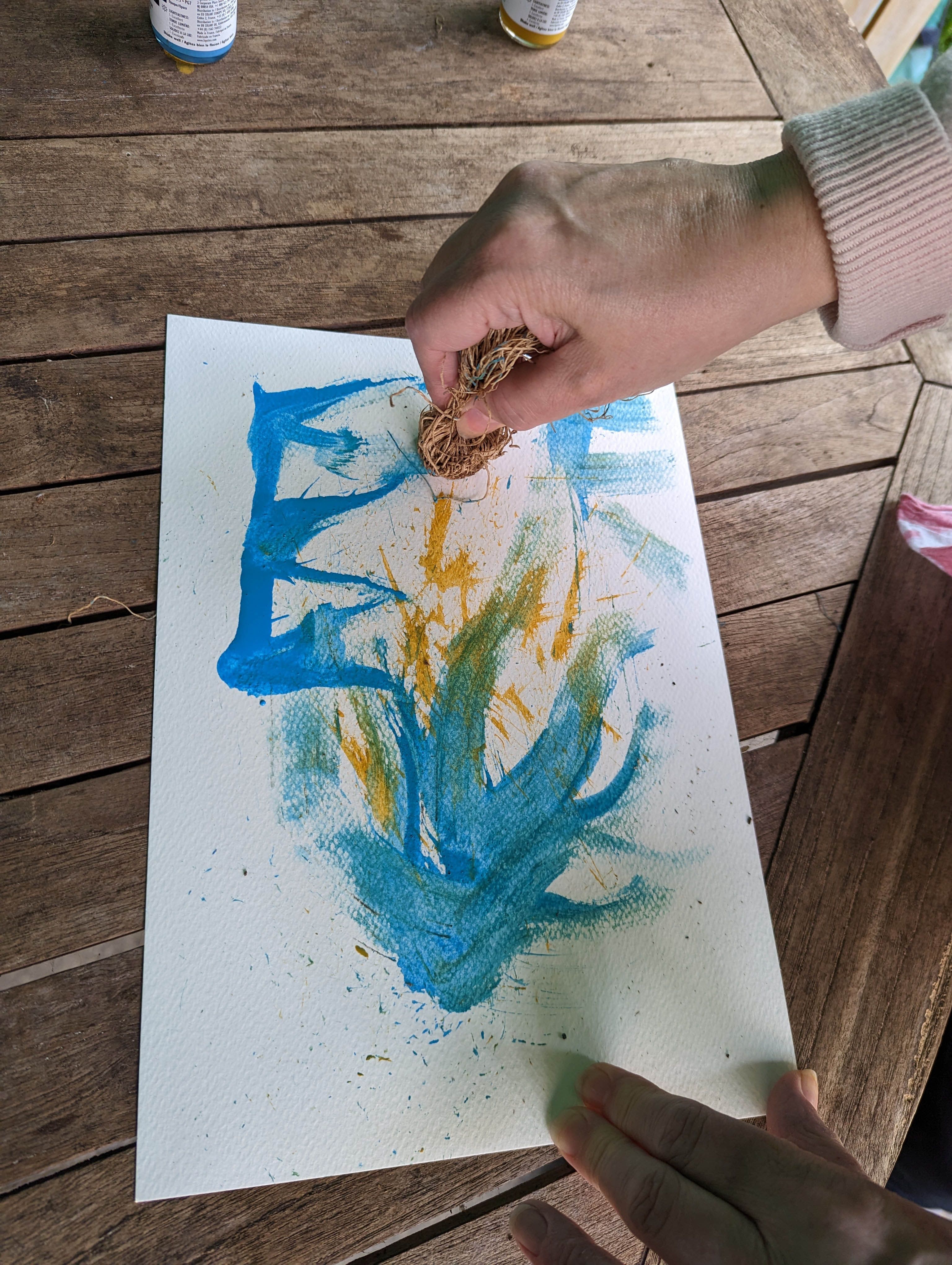 A hand applying paint to paper with some natural twine.