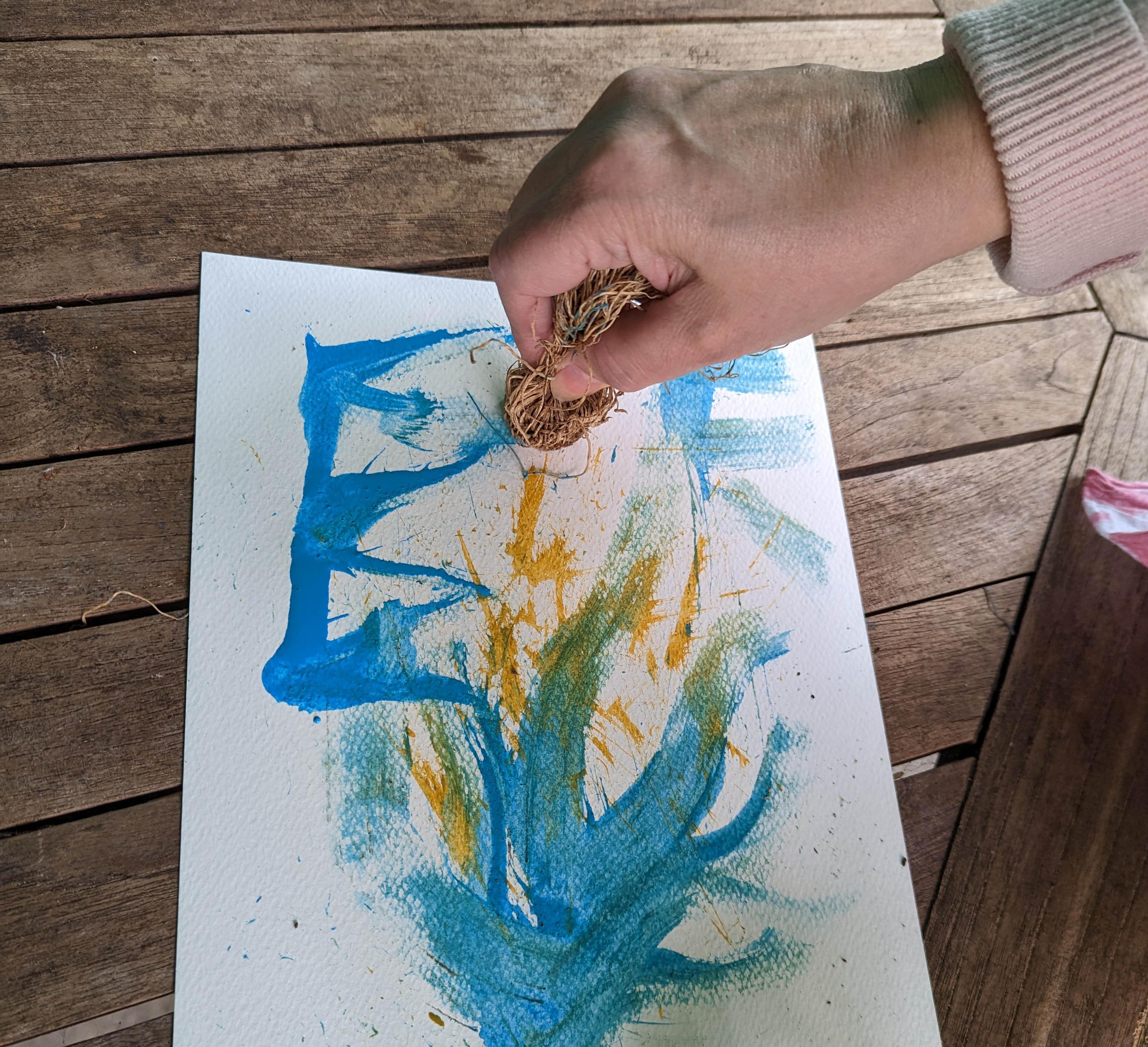 A hand applying paint to paper with some natural twine.