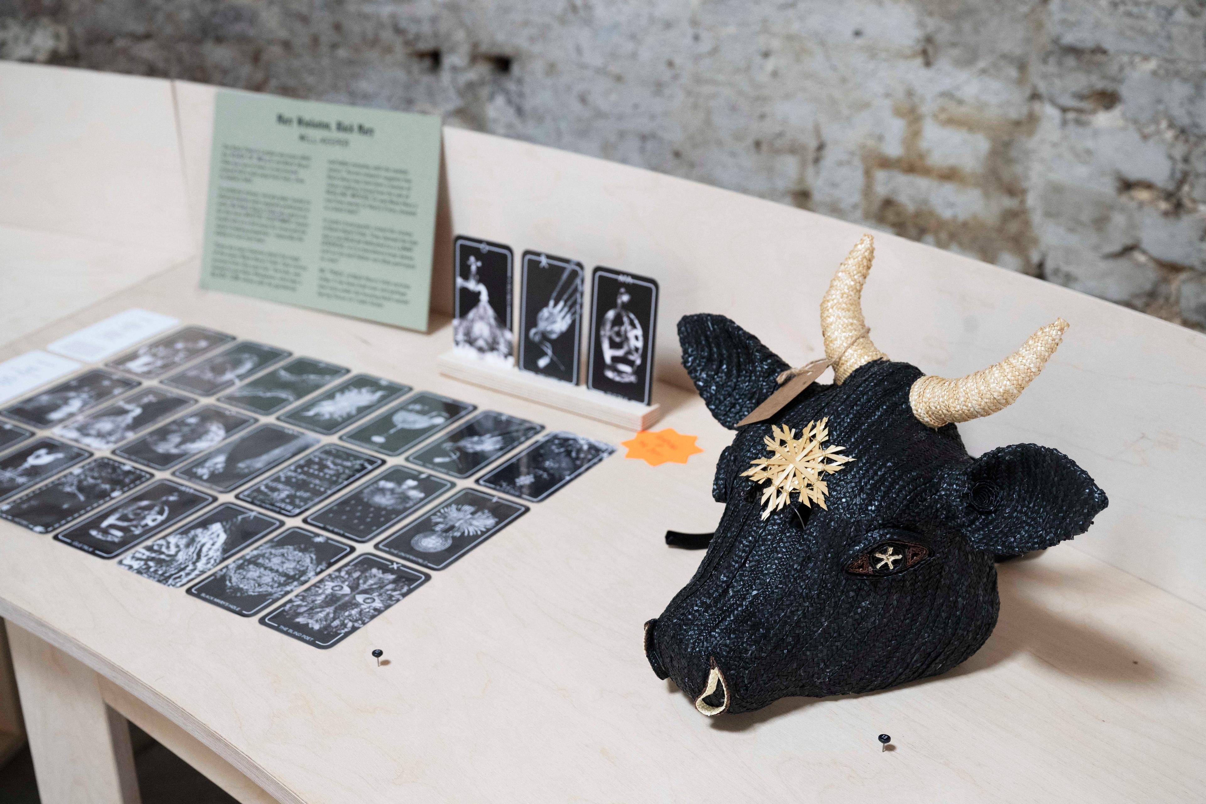 Photograph of a woven mask and tarot cards on a wooden platform.