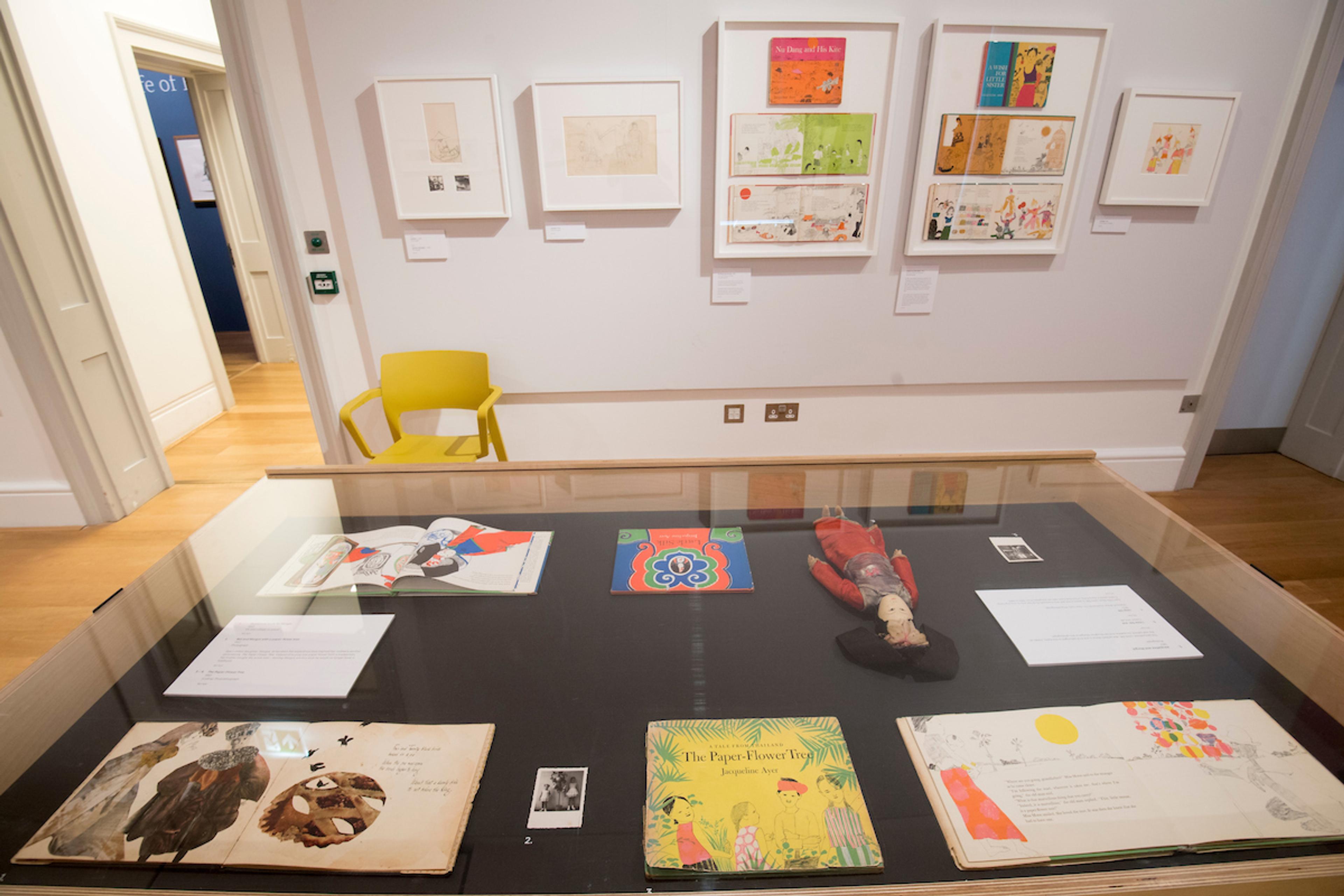 Inside an exhibition space with framed illustrations on the wall and displayed in a glass cabinet.