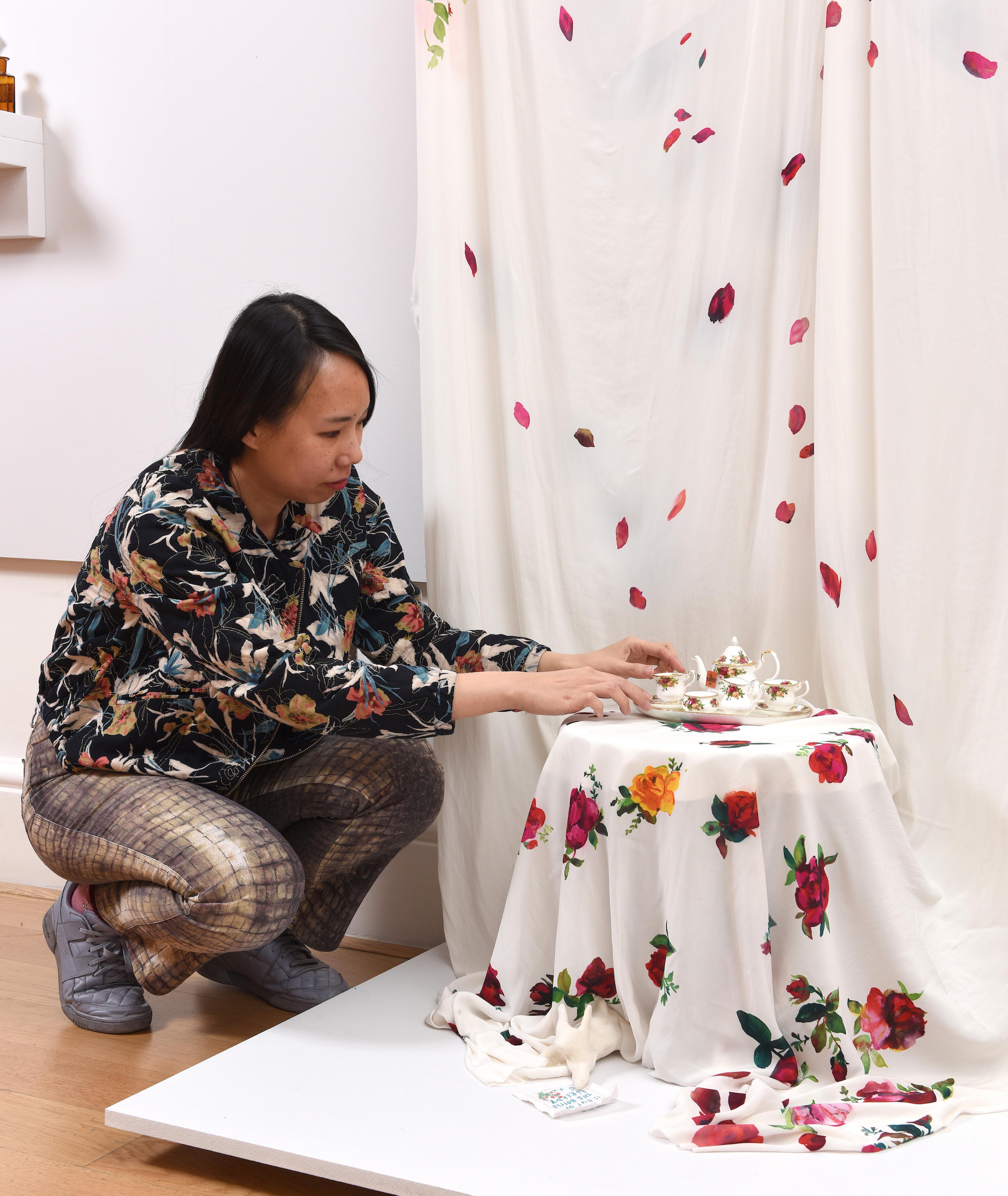 Photograph of a woman crouched down arranging a display of a tea set