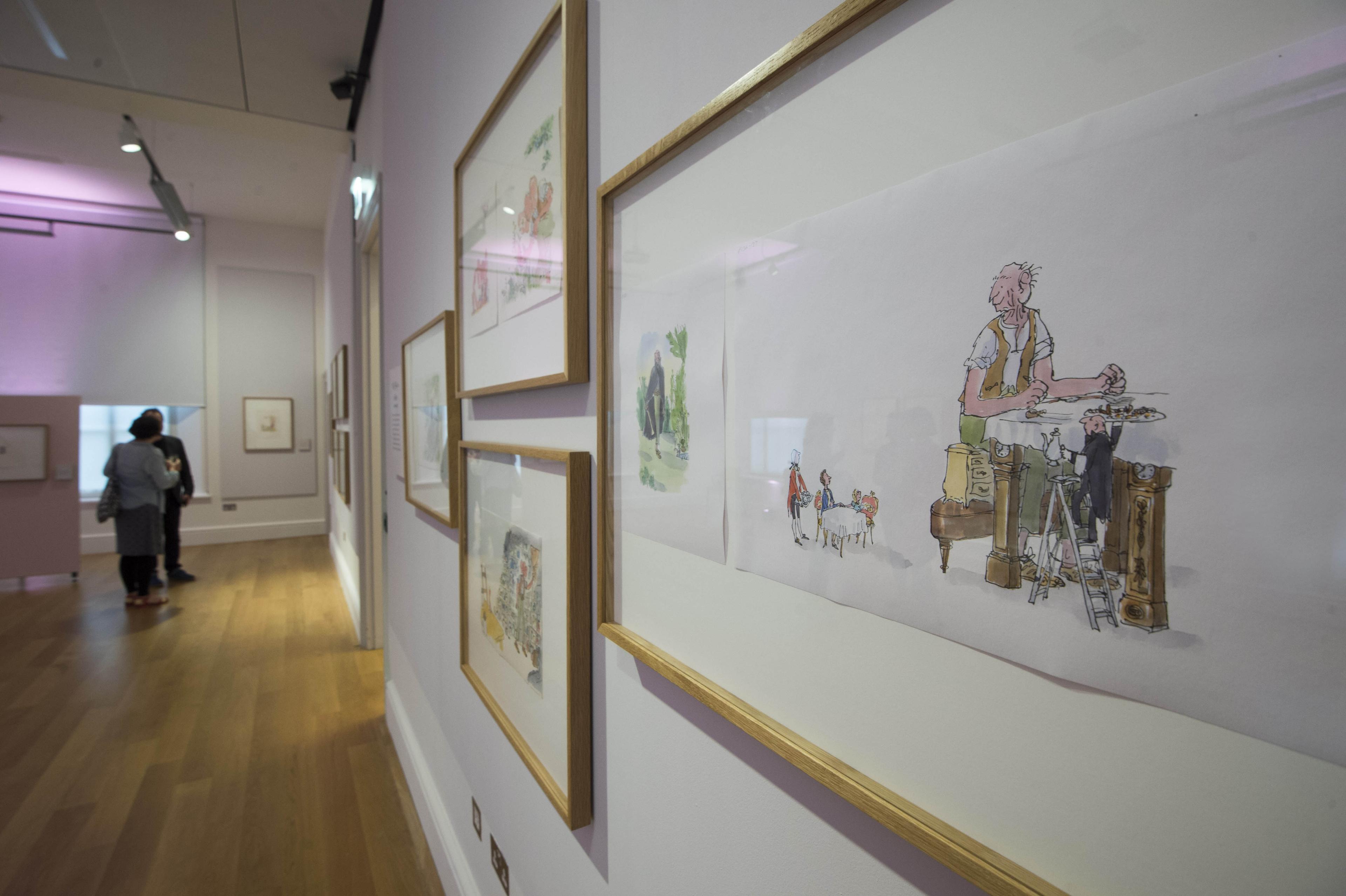 Two people in an exhibition space with framed illustrations on the wall.