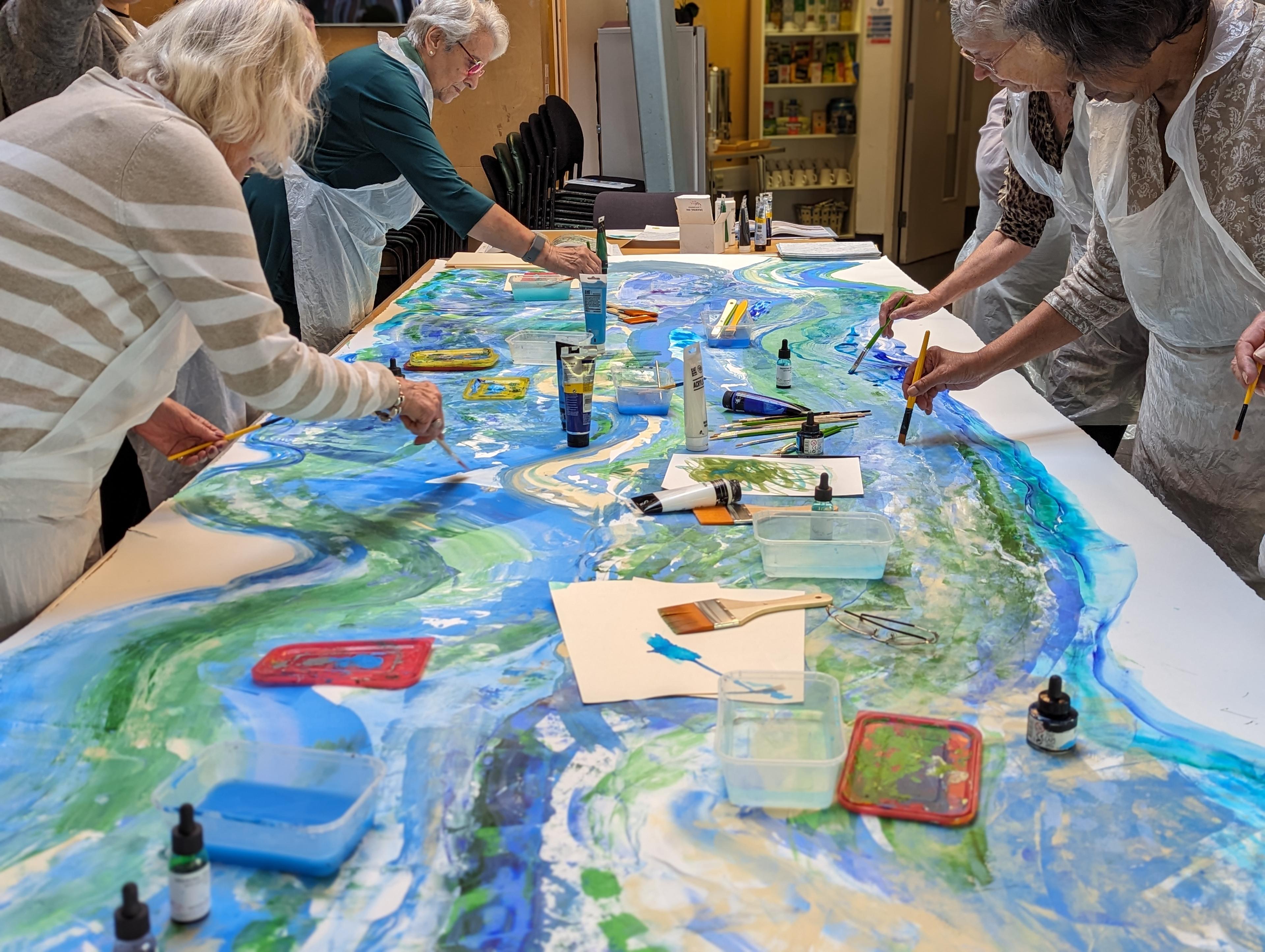 A group of four older people painting water on a single, large sheet of paper.