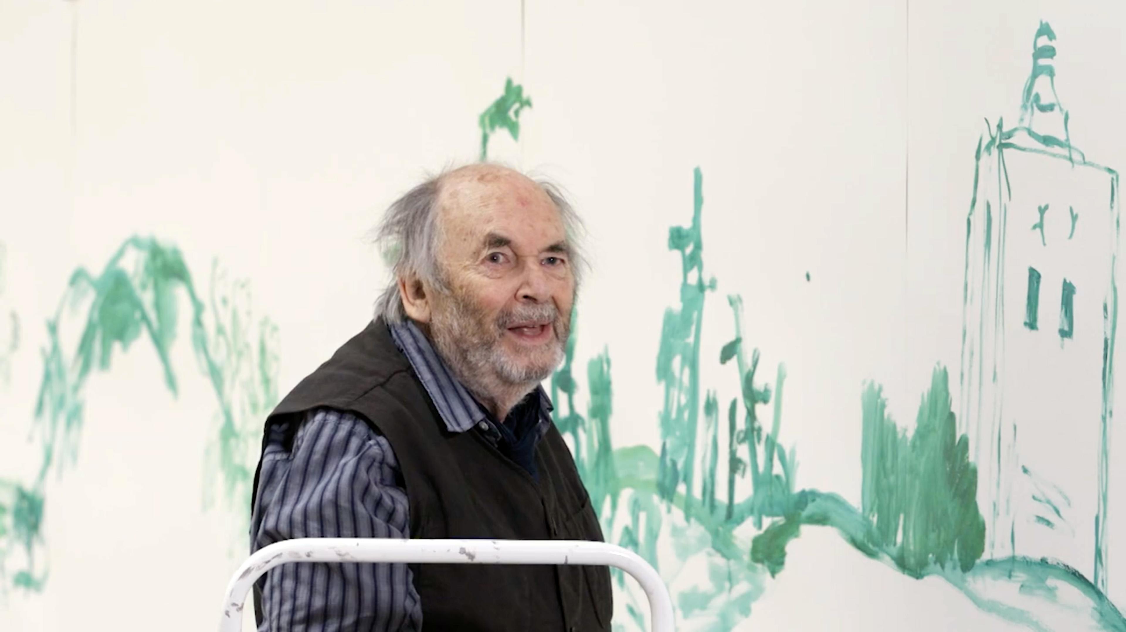 Photograph of Quentin Blake in front of a green illustration painted onto the wall.